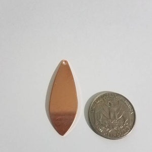 May include: A copper-colored teardrop-shaped pendant with a hole at the top. The pendant is about the size of a US quarter.