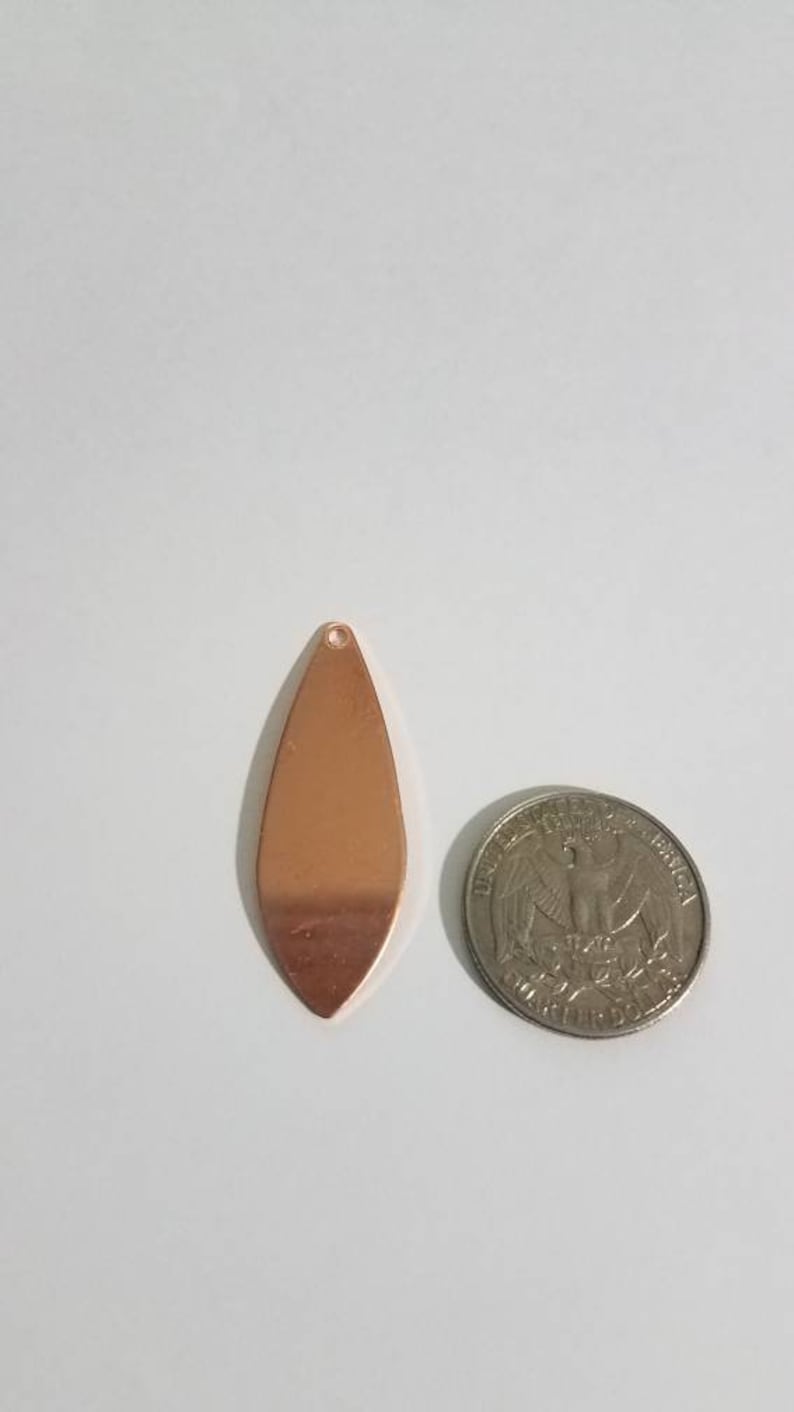 May include: A copper-colored teardrop-shaped pendant with a hole at the top. The pendant is about the size of a US quarter.
