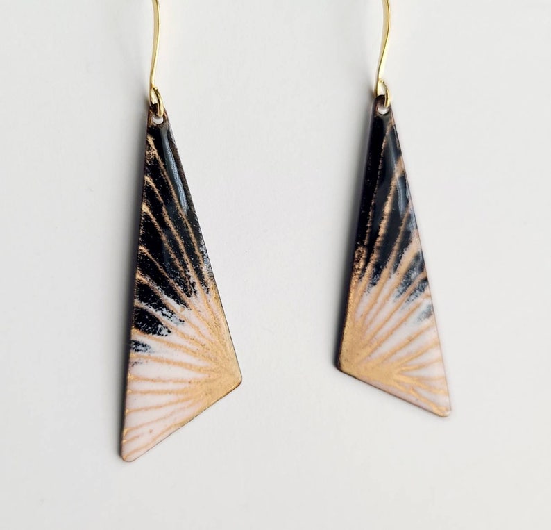 May include: A pair of gold dangle earrings with black and white enamel triangles. The triangles have a sunburst design with gold accents.