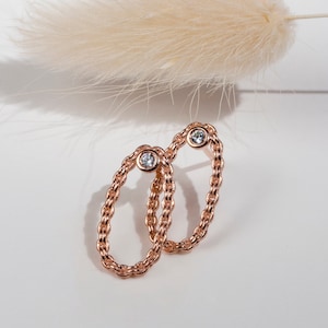 May include: A pair of rose gold oval earrings with a single clear stone in each earring. The earrings are made of a chain-like design.