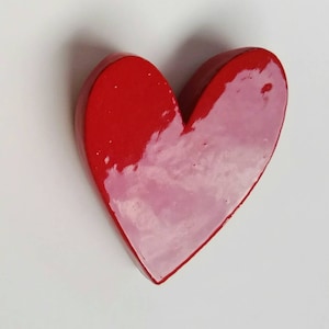 May include: A red heart-shaped ceramic ornament with a glossy finish. The heart has a lighter pink hue in the centre, creating a gradient effect.
