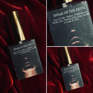 K&ouml;nnte beinhalten: Eine Glasflasche Parf&uuml;m mit einem goldenen Verschluss und einem schwarzen Etikett. Das Etikett lautet "Speak of the Devil" und listet die Duftnoten auf: Gealterte Eiche, Bernstein, Schwefel, Moschus, Trockenes R&auml;ucherholz, Vanille, Sahne & Kiefer.