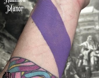 May include: A close-up of a person's arm with a swatch of purple paint applied to the skin. The text "Haunted Manor" is visible in the top left corner of the image.