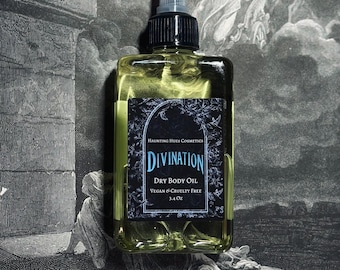 May include: A clear glass bottle with a black cap and label. The label reads "Haunting Hues Cosmetics Divination Dry Body Oil Vegan & Cruelty Free 3.4 oz".