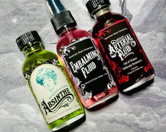 May include: Three glass bottles of cosmetic products with black caps. The bottles are labeled "Absinthe Glycolic Acid Toner", "Embalming Fluid Mini Setting Spray", and "Arterial Fluid Oil & Water Makeup Remover". The bottles have a vintage aesthetic.