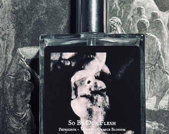 May include: A glass bottle of perfume with a silver cap. The label reads "So Be Our Flesh" and lists the notes as "Petrichor - Violets - Orange Blossom".