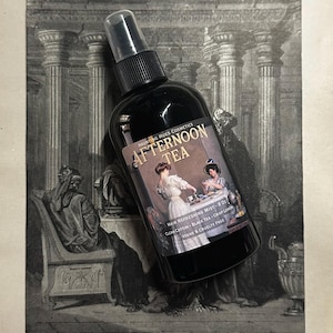 May include: A black bottle with a spray nozzle and a label that reads "Haunting Hues Cosmetics Afternoon Tea Hair Refreshing Mist - 8 oz Clean Cotton - Black Tea - Crisp Lemon Vegan & Cruelty Free".