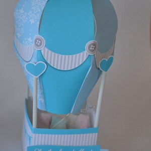 May include: A blue and white paper hot air balloon with a banner that reads "Oh... the places he'll go!" and a smaller banner that reads "Happy 1st Birthday Alex".