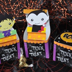 May include: Three Halloween treat boxes with different characters. The first box features a green monster with a purple shirt and the text "Trick or Treat". The second box features a vampire with a red cape and the text "Trick or Treat". The third box is a cube with the text "Boo!" and "Trick or Treat".