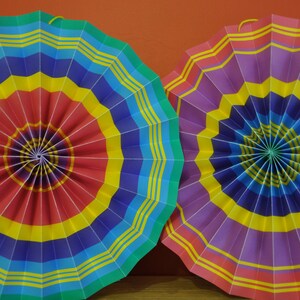 K&ouml;nnte beinhalten: Zwei bunte Papierf&auml;cher, einer mit roten, gelben, blauen und gr&uuml;nen Streifen und der andere mit violetten, gelben, blauen und roten Streifen.