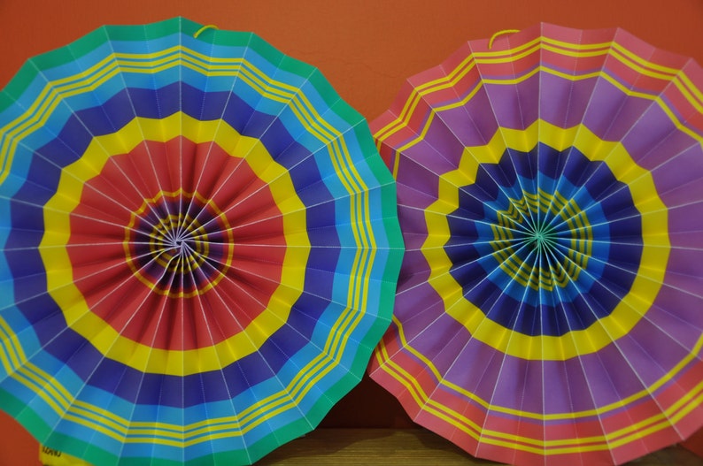 K&ouml;nnte beinhalten: Zwei bunte Papierf&auml;cher, einer mit roten, gelben, blauen und gr&uuml;nen Streifen und der andere mit violetten, gelben, blauen und roten Streifen.