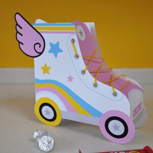 Peut inclure: Une bo&icirc;te de faveur de f&ecirc;te en forme de patin &agrave; roulettes rose et blanche avec un motif ray&eacute; jaune, rose et bleu. La bo&icirc;te a une aile rose sur le c&ocirc;t&eacute; et une &eacute;toile jaune sur le devant. La bo&icirc;te est en carton et a une petite ouverture sur le dessus pour le remplissage.