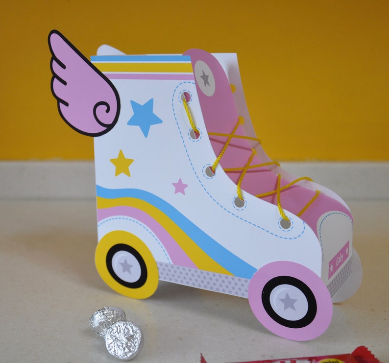 Peut inclure: Une bo&icirc;te de faveur de f&ecirc;te en forme de patin &agrave; roulettes rose et blanche avec un motif ray&eacute; jaune, rose et bleu. La bo&icirc;te a une aile rose sur le c&ocirc;t&eacute; et une &eacute;toile jaune sur le devant. La bo&icirc;te est en carton et a une petite ouverture sur le dessus pour le remplissage.
