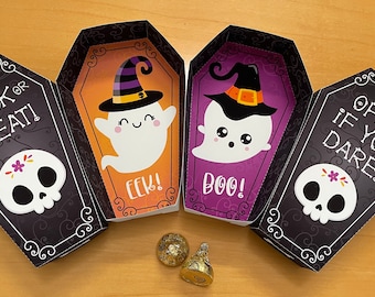 May include: Four black and white coffin-shaped boxes with a skull and the text "Trick or Treat!" on the front. The boxes are open to reveal a ghost with a witch's hat and the text "Boo!" and "Eek!" on the inside. Two gold chocolate coins are in front of the boxes.