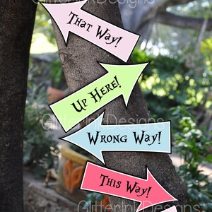May include: Six colorful arrow signs with whimsical text attached to a tree trunk. The signs read "Tea Party!", "That Way!", "Up Here!", "Wrong Way!", "This Way!" and "We're All Mad Here!"