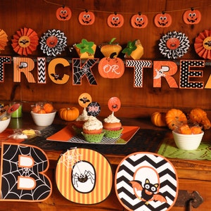 May include: A Halloween party table setting with orange and black decorations. The table is decorated with a banner that says "Trick or Treat", cupcakes with orange and black frosting, and bowls of candy. There are also orange and black paper fans and pumpkins.