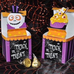 May include: Two Halloween treat boxes with a trick or treat theme. One box features a skeleton wearing a top hat and the other features a cupcake with googly eyes. Both boxes have a purple, black, and orange color scheme.