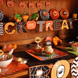 May include: A Halloween party table setting with orange and black decorations. The table is decorated with a "Trick or Treat" banner, cupcakes, and candy.