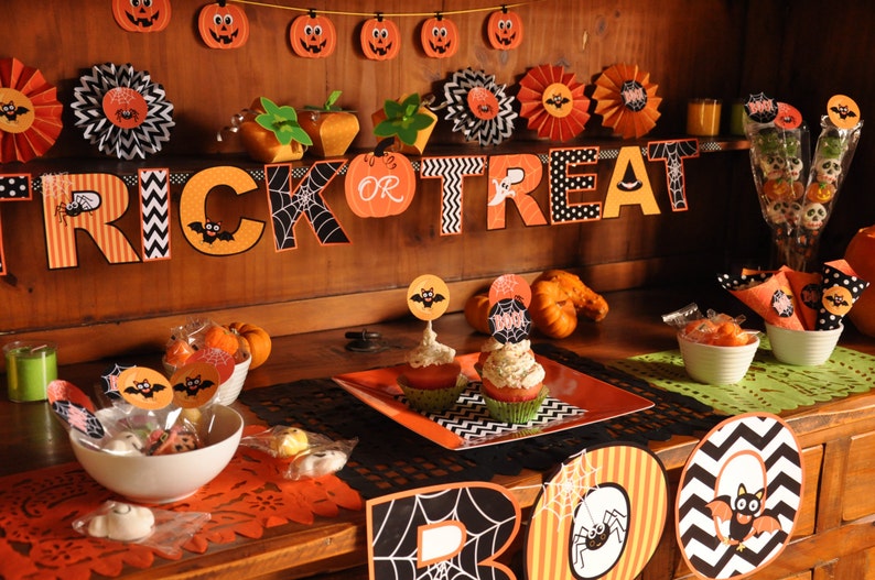 May include: A Halloween party table setting with orange and black decorations. The table is decorated with a "Trick or Treat" banner, cupcakes, and candy.