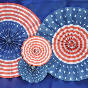 Könnte beinhalten: Drei Papierfächer in Rot, Weiß und Blau mit einem Sternenmuster. Die Fächer sind gefaltet und haben eine kreisförmige Form.