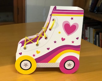 Può includere: Una scatola regalo decorativa a forma di pattino a rotelle. La scatola è bianca con un cuore rosa, stelle e un design arcobaleno. Ha lacci gialli e ruote con una stella al centro. Il design generale è giocoso e colorato.