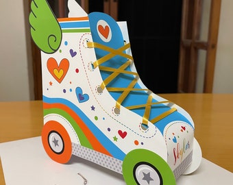 Può includere: Una scatola di festa in cartone a forma di pattino a rotelle colorata con un'ala verde, lacci blu e il testo "Sky Car".