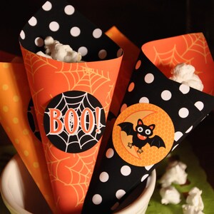 May include: Three orange and black Halloween popcorn cones with spiderweb and polka dot patterns. One cone has a black circle with the word "BOO!" in white letters. Another cone has a black circle with a cartoon bat and a crescent moon.