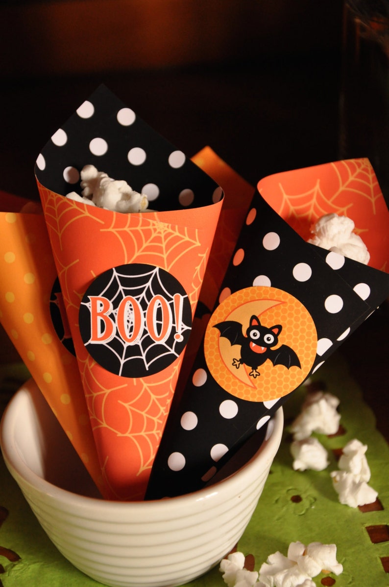 May include: Three orange and black Halloween popcorn cones with spiderweb and polka dot patterns. One cone has a black circle with the word "BOO!" in white letters. Another cone has a black circle with a cartoon bat and a crescent moon.