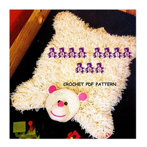Puede incluir: Patrón de crochet para una alfombra de oso beige con nariz rosa y ojos negros. La alfombra está rodeada de letras de fieltro morado que deletrean "Bare Skin Rug".