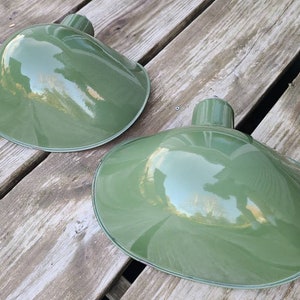 May include: Two green metal lampshades with a glossy finish. The lampshades are shaped like a shallow bowl and have a slight curve to them.