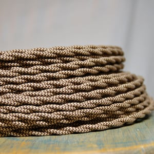 May include: Close-up of a brown and beige braided cord, coiled in a spiral shape. The cord is made of a woven fabric with a chevron pattern.