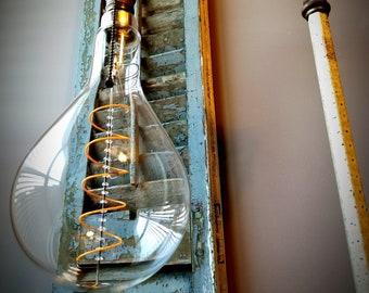 May include: A vintage-style light fixture with a clear glass bulb and a coiled filament. The fixture is attached to a weathered wooden shutter with a metal arm.