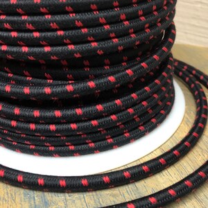 Könnte beinhalten: Nahaufnahme eines schwarzen und roten Stromkabels mit einer strukturierten Oberfläche. Das Kabel ist um eine weiße Spule gewickelt.