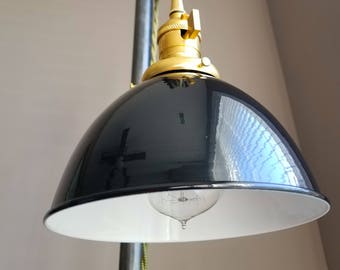 Puede incluir: Una lámpara colgante de estilo industrial en blanco y negro con una toma de corriente dorada y un sistema de poleas. La luz cuelga de una tubería de metal.
