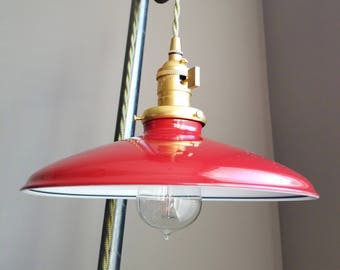 Puede incluir: Una lámpara colgante de metal roja con un interior blanco y una toma de corriente dorada. La luz está suspendida de una cuerda verde y un sistema de poleas vintage.