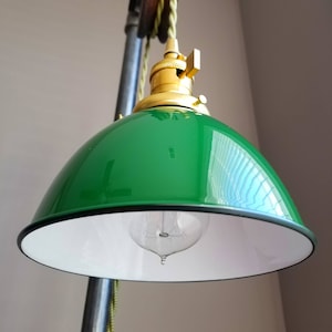 Puede incluir: Una lámpara colgante de estilo industrial con una pantalla verde y blanca, una toma de latón y un sistema de poleas.