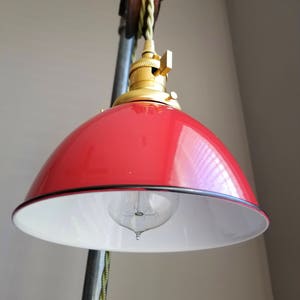 Puede incluir: Una lámpara colgante de estilo industrial con una pantalla roja y blanca, una toma de metal dorado y un sistema de polea.