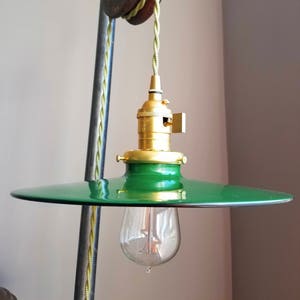 Puede incluir: Una lámpara colgante de metal verde con una toma de latón y una bombilla transparente. La luz está suspendida de un cordón verde que se enhebra a través de una polea vintage.
