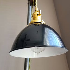 Puede incluir: Una lámpara colgante de estilo industrial en blanco y negro con una toma de corriente dorada y un sistema de poleas. La luz cuelga de una tubería de metal.