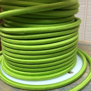 Może przedstawiać: Szpula zielonego przewodu elektrycznego, ciasno nawiniętego w spiralę. Przewód jest gładki i ma lekko fakturowaną powierzchnię.