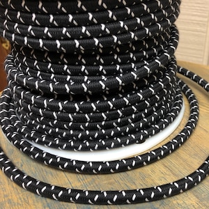 Könnte beinhalten: Eine Spule mit schwarzem und weißem Stromkabel mit einem weißen Zickzackmuster. Das Kabel ist fest um die Spule gewickelt.