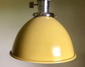 Puede incluir: Una lámpara colgante de metal amarilla con un casquillo plateado y un interruptor de encendido/apagado simple. La luz tiene una pantalla en forma de cúpula.