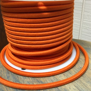 Puede incluir: Una bobina de cable eléctrico naranja. El cable está enrollado firmemente alrededor de la bobina y está listo para ser utilizado en proyectos eléctricos.