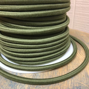 Może przedstawiać: Szpula zielonego przewodu elektrycznego, ciasno nawinięta w spiralę. Przewód jest ciemno oliwkowo zielony i ma gładką, lekko fakturowaną powierzchnię.