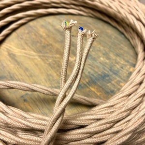May include: Close-up of a spool of beige twisted electrical cord. The cord is made of fabric and has three wires inside. The wires are visible at the end of the cord.
