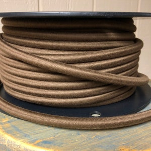 May include: A spool of brown cord wound tightly around a black plastic spool. The cord is a dark brown color and has a smooth texture.