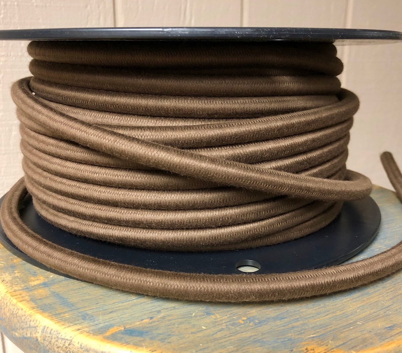 May include: A spool of brown cord wound tightly around a black plastic spool. The cord is a dark brown color and has a smooth texture.