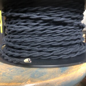 May include: A spool of black braided electrical cord. The cord is wound tightly around the spool and is ready to be used for electrical projects.