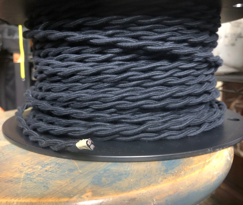 May include: A spool of black braided electrical cord. The cord is wound tightly around the spool and is ready to be used for electrical projects.