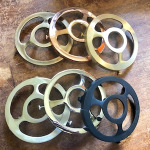 May include: Assortment of six metal lampshade rings in various finishes, including silver, gold, and black. The rings are circular in shape with a central opening and multiple cutouts around the edge.